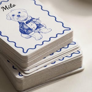May include: A stack of white rectangular cards with a blue wavy border. The top card features a blue ink sketch of a small dog wearing a tuxedo and a bow tie, with the name Milo printed in black script in the upper left corner of the card.