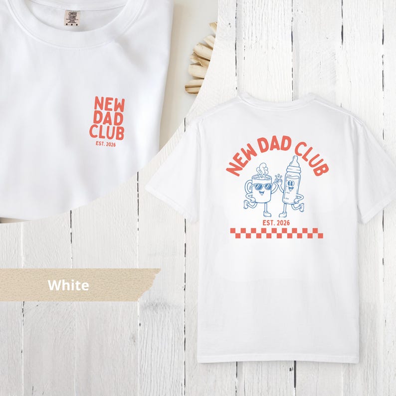 May include: White t-shirt with "NEW DAD CLUB" in red text on the front and back. The back features a cartoon coffee cup and baby bottle with sunglasses, and the text "EST. 2026". A red and white checkered pattern is at the bottom.