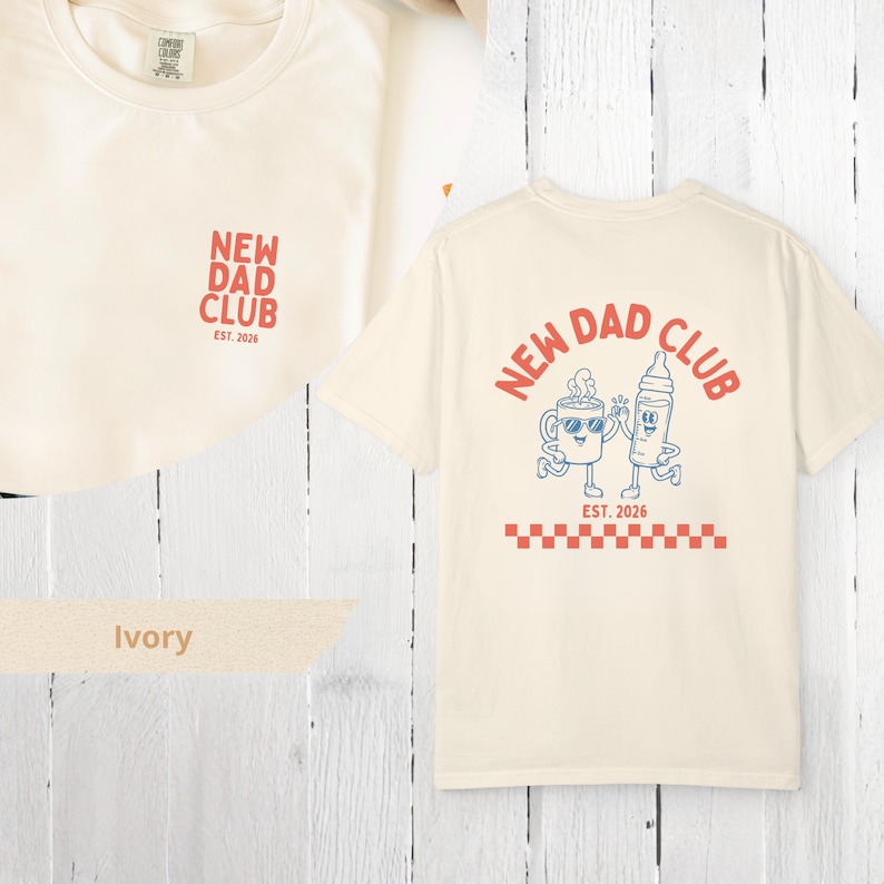 May include: Ivory-colored t-shirts with the text "NEW DAD CLUB" in red and blue. The front of the shirt has the text "NEW DAD CLUB" in red. The back of the shirt has a graphic of a coffee cup and a baby bottle.