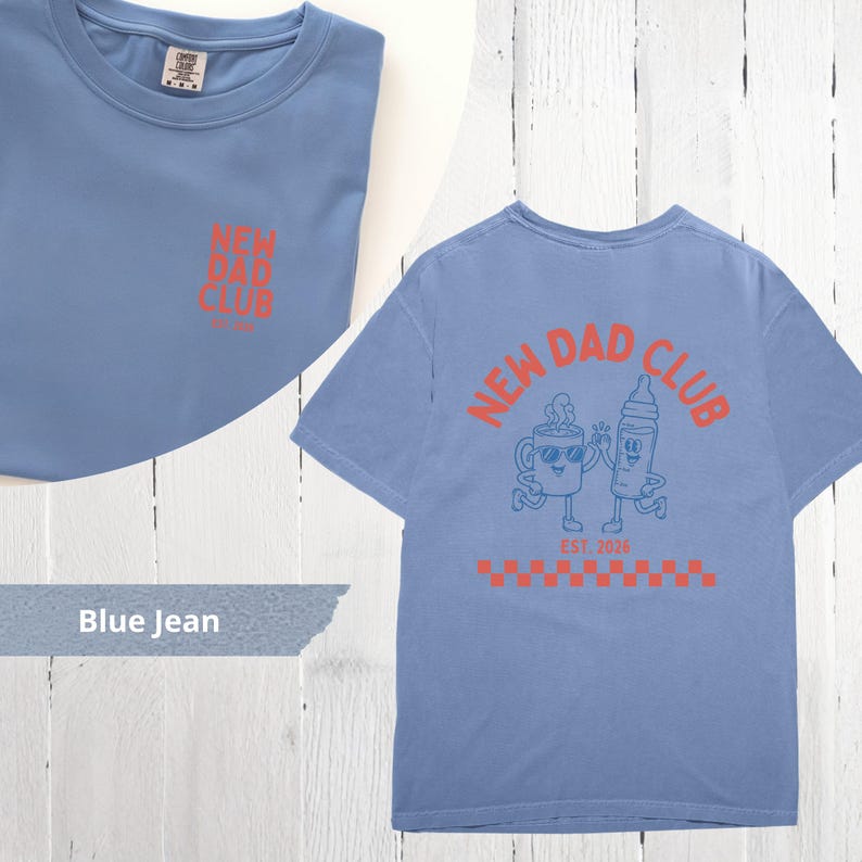 May include: Blue jean-colored t-shirt with the text "NEW DAD CLUB" in orange on the front and back. The back design features a coffee cup and baby bottle cartoon characters. The shirt has a crew neck and short sleeves.