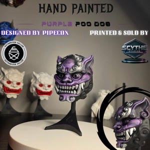 May include: Hand-painted purple Foo Dog mask on a black stand. The mask features intricate details, including sharp teeth and a fierce expression. The design is by PIPECOX and printed by SCYTHE Studios. Additional Foo Dog masks are visible in the background.