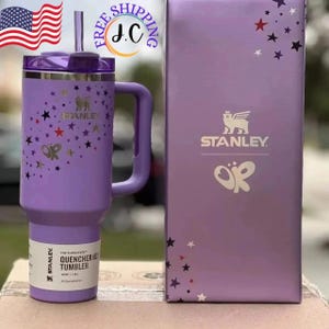 Puede incluir: Un vaso Stanley Quencher H2.0 FlowState morado con asa, pajita y tapa. El vaso est&aacute; decorado con estrellas doradas y un dise&ntilde;o de mariposa. La caja a juego tiene el logotipo de Stanley y dise&ntilde;os de estrellas.