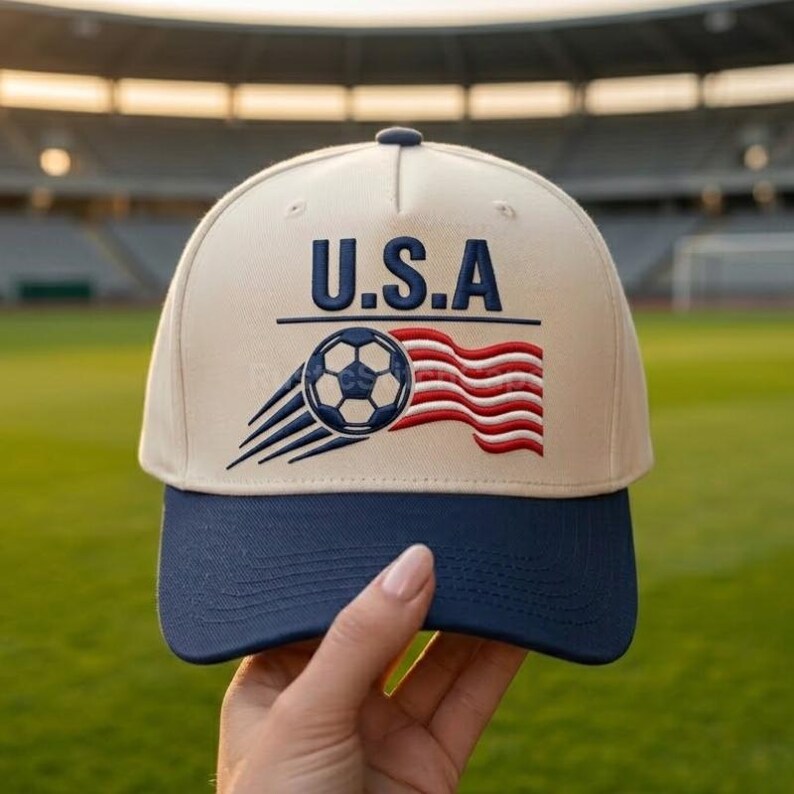 Peut inclure: Une casquette de baseball beige avec une visi&egrave;re bleu fonc&eacute;. L'avant pr&eacute;sente le texte U.S.A. en lettres bleu fonc&eacute; au-dessus d'un motif brod&eacute; d'un ballon de football avec des lignes de mouvement et un drapeau rouge et blanc ondul&eacute;.