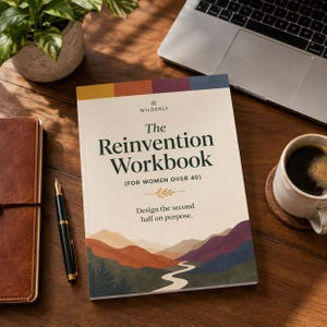 Op de afbeelding: Een werkboek getiteld "The Reinvention Workbook" met de tekst "Design the second half on purpose." Het boek ligt op een houten bureau naast een laptop, een koffiekopje, een pen en een leren notitieboek. Een plant in een pot staat op de achtergrond.