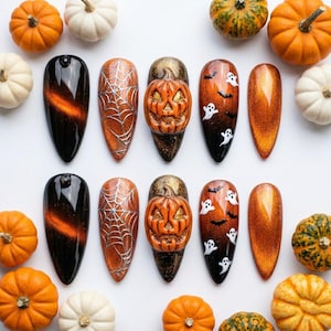 May include: A collection of Halloween-themed nail art designs. The designs include a black and orange gradient, a silver spiderweb, a 3D pumpkin, and ghosts with bats. The nails are surrounded by orange and white pumpkins.