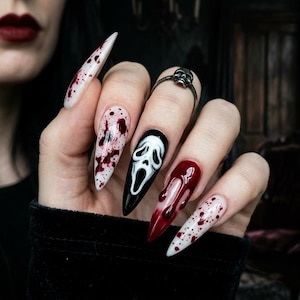 May include: Long, pointed acrylic nails with a Halloween theme. Designs include a Scream mask, blood splatter, and dripping blood effects. A silver skull ring is also visible.