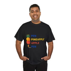 Op de afbeelding: Zwart t-shirt met een kleurrijke afbeelding van een ananas, appel en pen. De tekst "PEN PINEAPPLE APPLE PEN" staat in geel, rood en blauw. Een casual kledingstuk voor dagelijks gebruik.