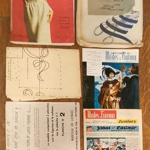 Può includere: Una collezione di riviste e modelli di cucito vintage "Modes et Travaux". Le riviste presentano copertine con donne in abito, e i modelli includono illustrazioni di cappotti e altri capi di abbigliamento. La tavolozza dei colori comprende rosso, bianco e beige.