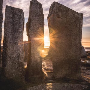 Puede incluir: Un paisaje escénico con grandes estructuras de piedra erosionada recortadas contra una puesta de sol. Los rayos del sol atraviesan los huecos entre las piedras, creando una escena dramática y hermosa. El cielo está lleno de nubes.