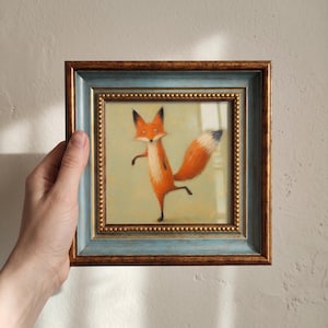 Peut inclure: Une peinture carrée encadrée représentant un renard orange stylisé avec une queue à bout blanc, debout sur une patte. Le cadre est composé d'une bordure intérieure bleue et d'un bord extérieur brun foncé, orné d'une rangée de petites perles dorées.