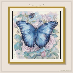 Op de afbeelding: Een ingelijst kruissteekontwerp met een grote blauwe vlinder met ingewikkelde vleugelpatronen, tegen een achtergrond van zachte roze en blauwe rozen en bladeren. Het kunstwerk zit in een gouden lijst.