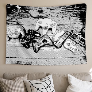May include: A black and white wall tapestry featuring a high-contrast graphic illustration of various vintage video game controllers arranged on a wooden surface. The design includes multiple handheld gamepads and a console controller.