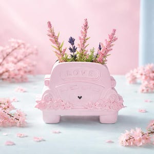 May include: A pink car-shaped planter with the word "LOVE" on the back. The planter is filled with pink and purple flowers. A small black heart is below the word "LOVE".