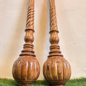 Op de afbeelding: Twee handgesneden houten oefenknotsen met een gepolijste bruine afwerking. Elke knots heeft een grote, ronde, gecanneleerde basis, een reeks gestapelde cirkelvormige ringen en een lange, slanke steel met een spiraalvormig, gedraaid ontwerp.