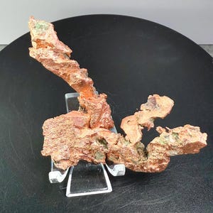May include: A natural copper specimen with a rough, textured surface and a reddish-brown color. The copper is displayed on a clear acrylic stand, set against a black circular base. The number "3" is in the top left corner.