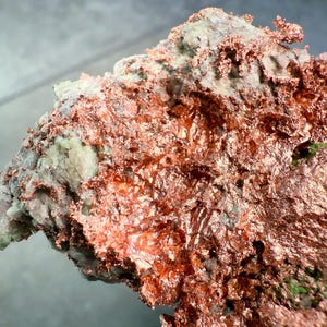 May include: A close-up of a copper ore specimen. The specimen displays a mix of textures and colors, with a prominent display of bright, metallic copper. The copper is layered and textured, contrasting with the lighter, mineral-rich matrix.