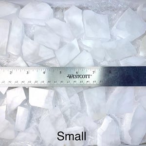 Pu&ograve; includere: Una collezione di piccoli pezzi di cristallo di quarzo bianco traslucido. Un righello di metallo, segnato in centimetri, &egrave; posto sui cristalli. La parola "Small" &egrave; scritta in basso nell'immagine.