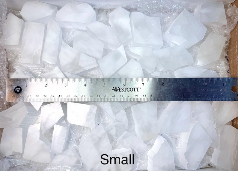 Pu&ograve; includere: Una collezione di piccoli pezzi di cristallo di quarzo bianco traslucido. Un righello di metallo, segnato in centimetri, &egrave; posto sui cristalli. La parola "Small" &egrave; scritta in basso nell'immagine.