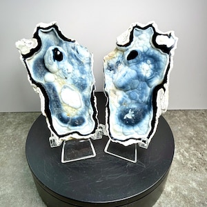 May include: Two matching, irregularly shaped, polished stone slabs with blue, white, and black patterns. The stones are displayed on clear stands atop a black rotating platform. The text "Set 1" is visible on the platform.