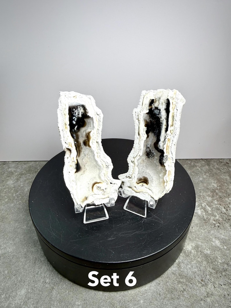 May include: Two white and black agate geodes, displayed on clear stands. The geodes have a crystalline exterior and a dark interior with intricate patterns. The set is labeled "Set 6" in white text.