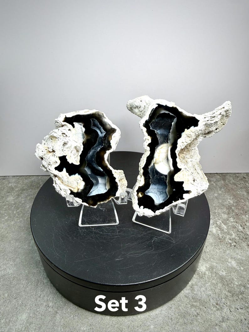 May include: Two geode halves with a black and white interior and a rough, textured exterior. The geodes are displayed on clear stands, set against a neutral background. The base is black, and the text "Set 3" is visible.