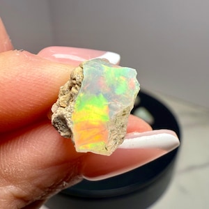 以下が含まれることがあります： 緑、黄色、オレンジなどの鮮やかな色を持つ、ラフカットのオパール原石。 オパールは、ニュートラルな背景に対して、その虹色の遊色効果を際立たせるように保持されています。 石は粗く、自然な質感を持っています。