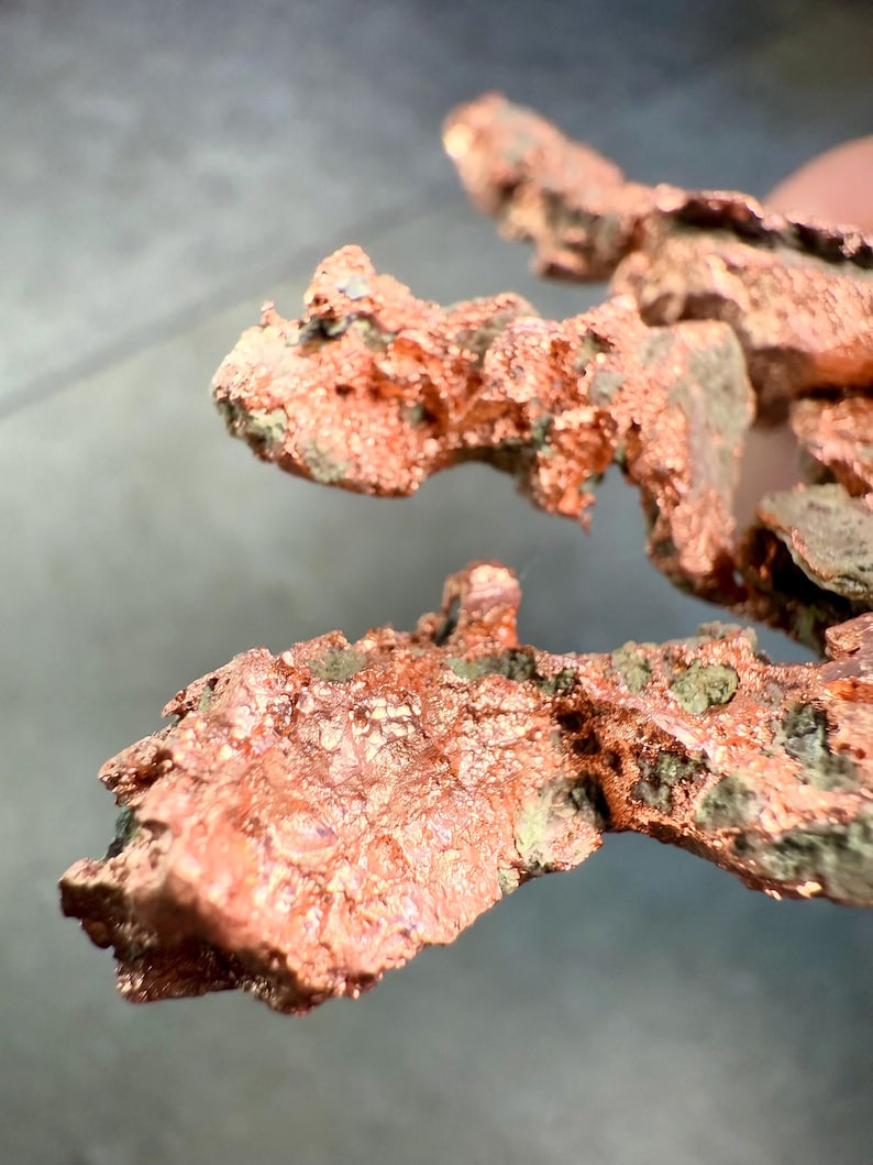 May include: Close-up of raw copper ore with a rough, textured surface. The copper has a reddish-brown color with patches of green and gray oxidation. The irregular shapes suggest a natural, unrefined state.