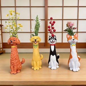 Könnte beinhalten: Vier hundeförmige Vasen in verschiedenen Farben und Designs, die künstliche Blumen halten. Die Vasen stehen auf einem Holztisch. Die Hunde haben lächelnde Gesichter und tragen Halsbänder oder Halstücher.
