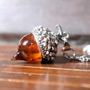May include: A silver acorn pendant necklace with a clear amber glass acorn. The necklace is on a silver chain.