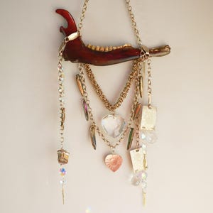 May include: A unique, handcrafted wall hanging featuring a dark brown jawbone. Gold-toned chains and various charms, including a clear heart pendant, hang from the jawbone. The piece incorporates crystals and metallic accents for added visual interest.