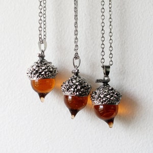 May include: Three silver acorn necklaces with amber glass accents. The acorns are detailed with textured metal and hang from silver chains.