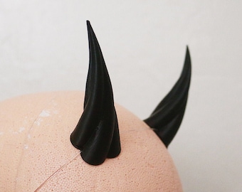 Könnte beinhalten: Ein Paar schwarze Teufelshörner aus Kunststoff, befestigt an einem Schaumstoffkopf.