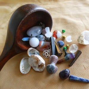 May include: A wooden bowl overflowing with a variety of crystals, stones, and other objects, including a pentagram charm, a seashell, and a clear quartz crystal.