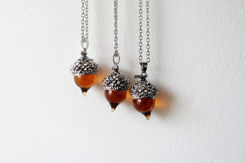 May include: Three silver acorn necklaces with amber glass accents. The acorns are detailed with textured metal and hang from silver chains.