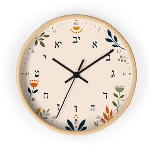May include: A round wall clock with a light beige face and a natural wood frame. The clock face features Hebrew numerals and floral designs in navy, orange, and green. Black clock hands indicate the time.