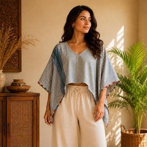 Op de afbeelding: Een lichtblauw en wit patroon V-hals poncho top met een donkerblauw zijpaneel en kleurrijke rand, gecombineerd met een beige broek met wijde pijpen en een elastische tailleband met trekkoord. De outfit bestaat uit een losvallende top en broek.