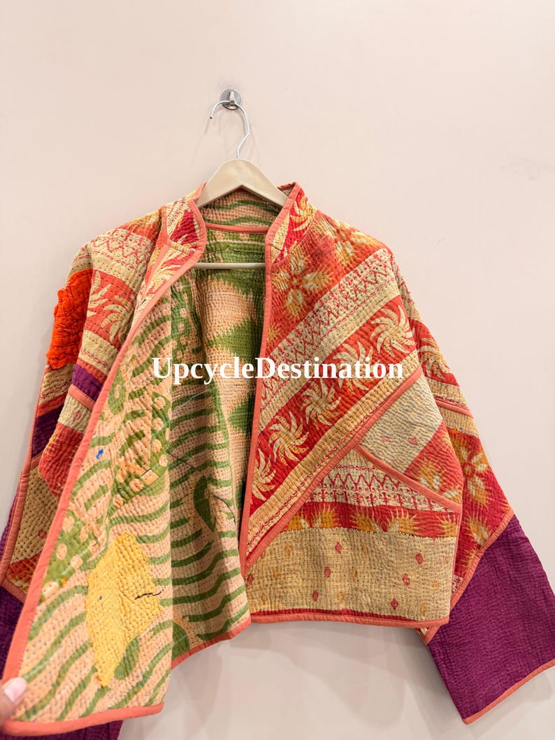 May include: A quilted jacket featuring a patchwork design with orange, green, yellow, and purple fabric panels. The garment has a mandarin collar, long sleeves, and visible kantha stitching throughout. The text UpcycleDestination is visible.