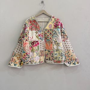 May include: A patchwork jacket with a V-neck and long sleeves. The jacket features a variety of floral and geometric patterns in shades of pink, yellow, green, and beige. The jacket is quilted and has a striped lining.