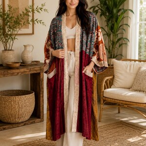 Könnte beinhalten: Ein langer Kimono mit offener Vorderseite und Patchwork-Design, bestehend aus tiefroten, senfgelben und blaugrünen Blumenmustern. Das Kleidungsstück verfügt über eine hellbeige gemusterte Borte an den Vorderkanten sowie zwei aufgesetzte Taschen.