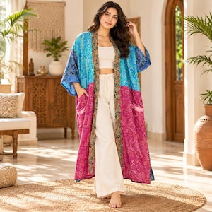 May include: A long, open-front kimono robe featuring a vibrant patchwork design with bright blue and magenta sections, accented by a dark green and gold paisley-patterned trim along the front edges and two large patch pockets on the front panels.