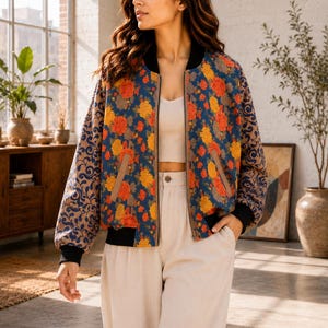 Puede incluir: Una chaqueta bomber con base azul y un vibrante estampado floral naranja y amarillo en los paneles frontales, contrastada por mangas color canela adornadas con un estampado de enredaderas azul oscuro, puños acanalados negros, cuello negro y cremallera.
