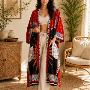 Puede incluir: Un kimono largo de frente abierto con un diseño de patchwork vibrante en secciones rojas, negras y blancas. La prenda muestra un gráfico de rayos de sol, patrones geométricos y motivos florales, con mangas anchas y dos bolsillos delanteros.