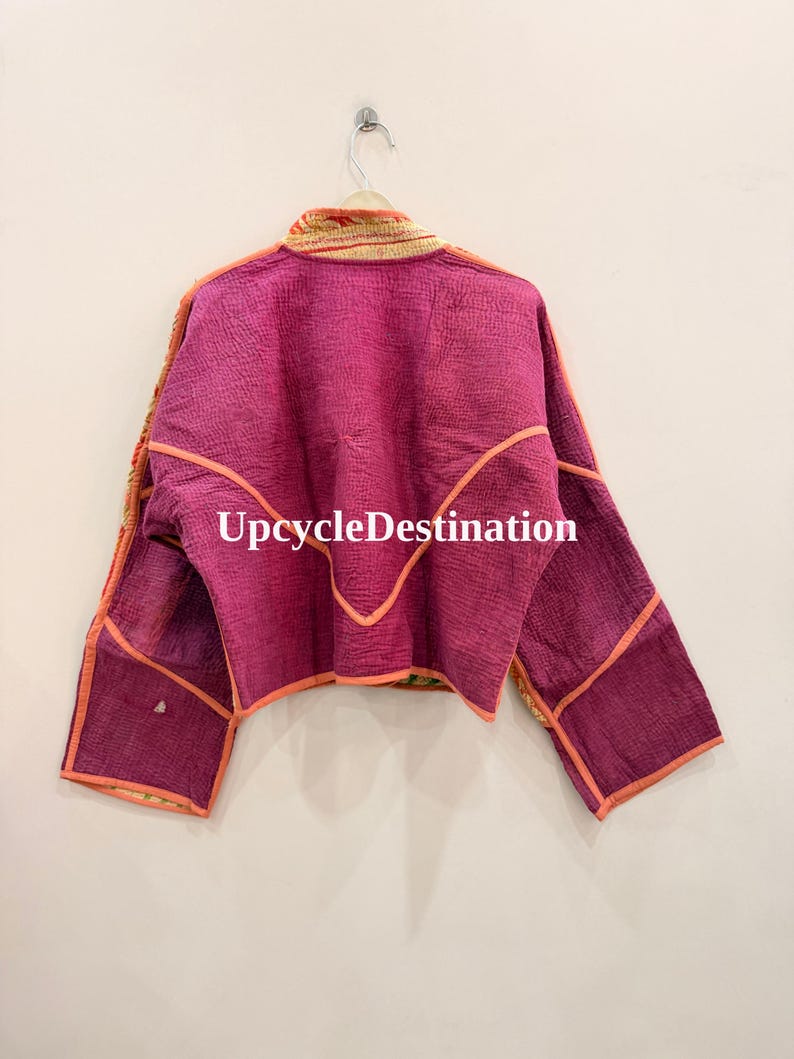 May include: A cropped jacket in a vibrant magenta hue featuring visible quilted stitching throughout. The garment has long sleeves, a high collar, and orange piping along the seams. The text UpcycleDestination is printed in white across the back.