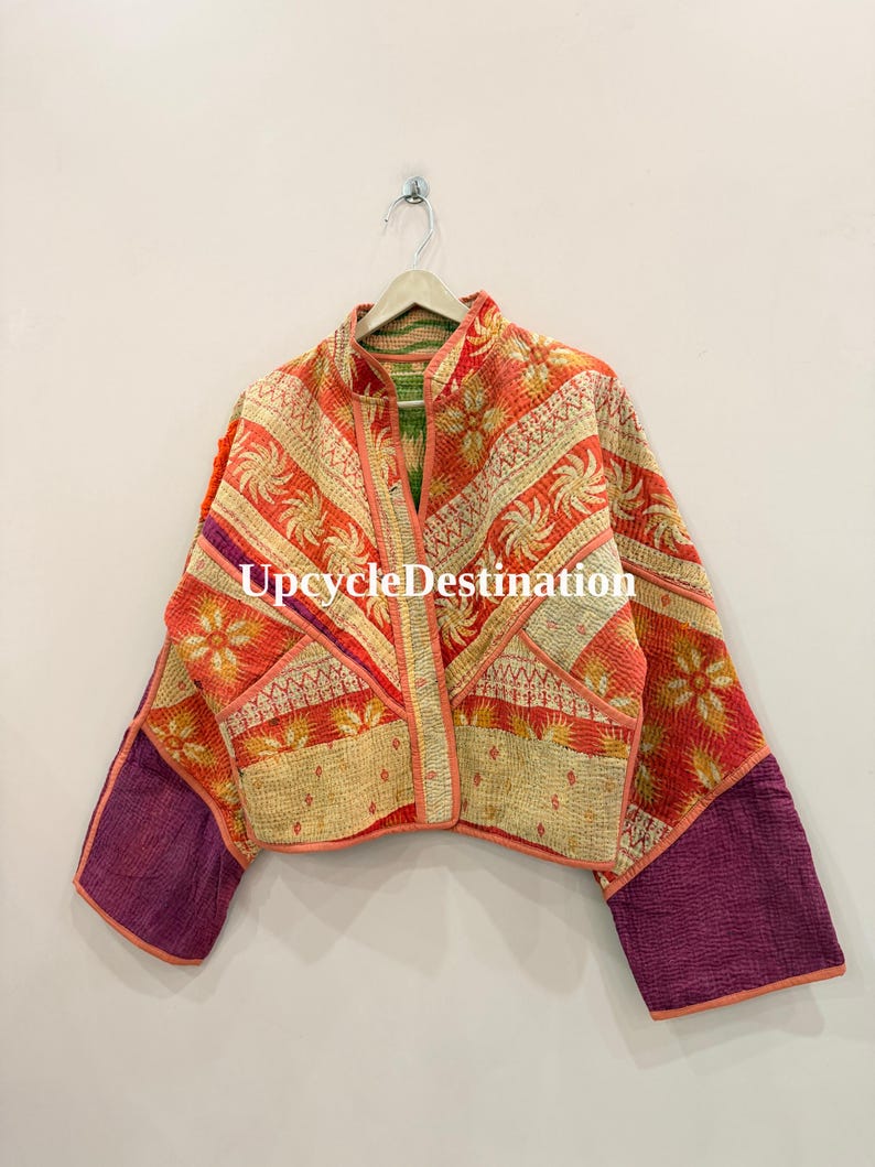 May include: A quilted jacket featuring a vibrant patchwork of orange, red, and cream floral patterns with contrasting solid purple sleeves. The garment has a mandarin collar, front pockets, and the text UpcycleDestination printed in white.