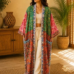 May include: A long, open-front kimono robe featuring a vibrant patchwork of paisley patterns in shades of green, red, and orange. The garment includes wide sleeves, two front patch pockets, and a contrasting blue and white patterned trim along the edges.