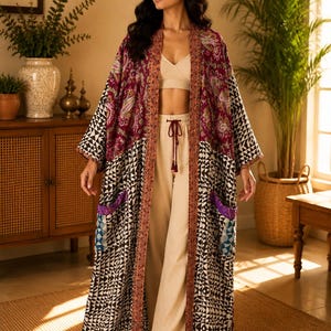 May include: A long, open-front duster robe featuring a patchwork design with a deep burgundy paisley upper section and a black and white geometric patterned lower section. The garment includes two front pockets and a decorative trim along the edges.