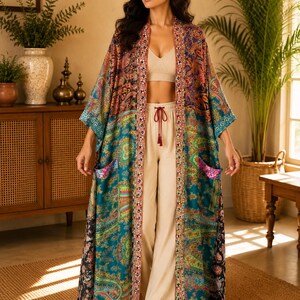 May include: A long, open-front kimono robe featuring a vibrant, multi-coloured paisley pattern in shades of teal, orange, and black. The garment includes two front patch pockets and a decorative, intricate border along the front opening and hem.