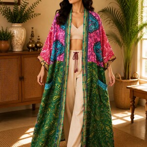 Może przedstawiać: Długi kimono z otwartym przodem o żywym, kolorowym wzorze. Górna część jest jaskraworóżowa w niebieskie wzory paisley, natomiast dolna część jest ciemnozielona ze skomplikowanymi złotymi i zielonymi motywami paisley oraz dwiema kieszeniami.
