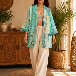 Puede incluir: Una chaqueta tipo kimono de patchwork en color turquesa claro con diversos patrones florales y geométricos en tonos azules, verdes y rosas. La chaqueta tiene mangas tres cuartos, frente abierto y un bolsillo visible en el lado izquierdo.
