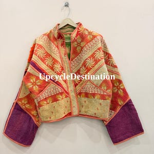 May include: A cropped jacket featuring a patchwork design with orange, red, and cream floral patterns, accented by solid purple sleeves and orange trim. The garment has a stand-up collar and is displayed on a hanger with the text UpcycleDestination.